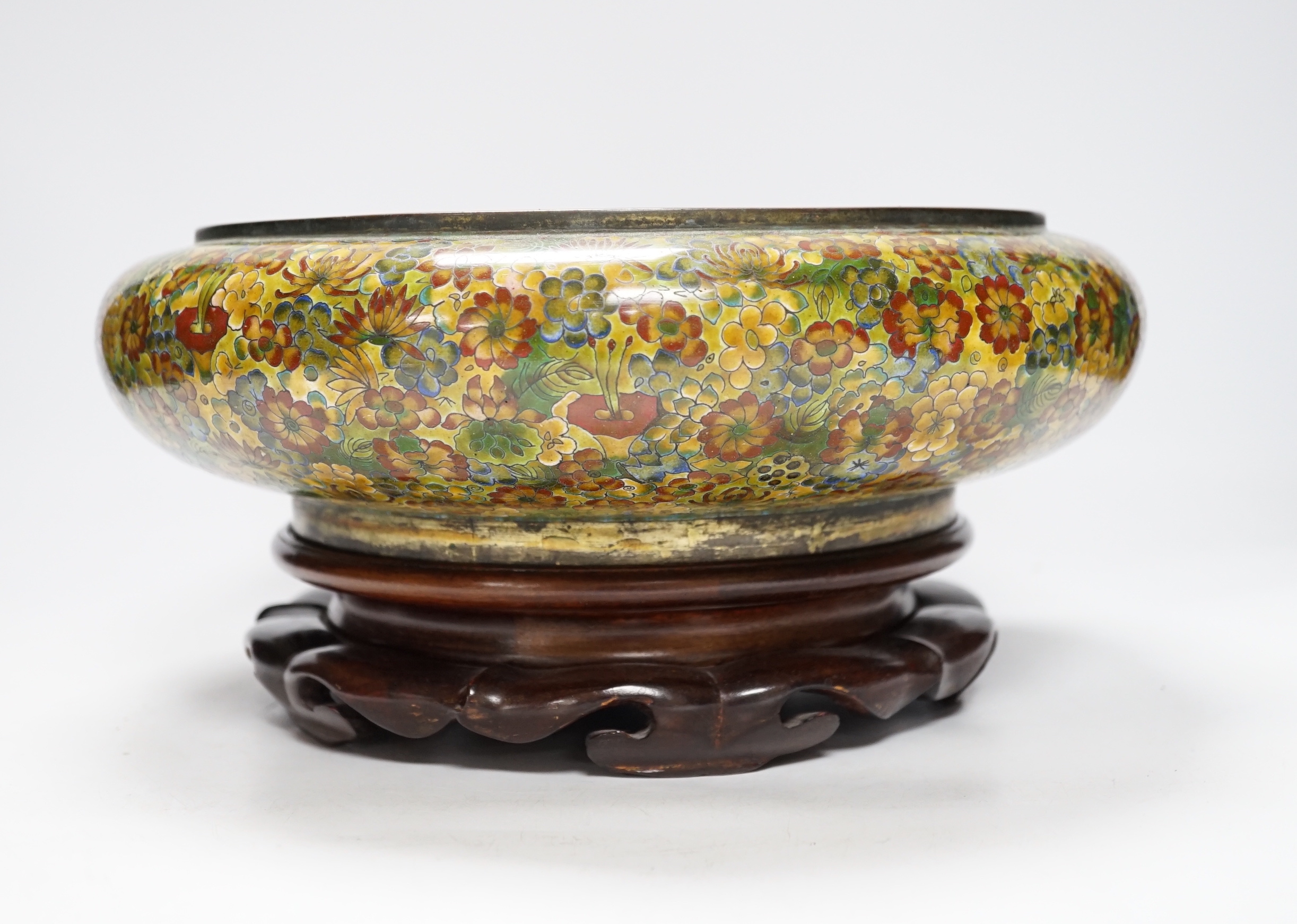 A Chinese circular cloisonné enamel bowl decorated with multi-coloured flowerheads on wooden stand, 30cm diameter